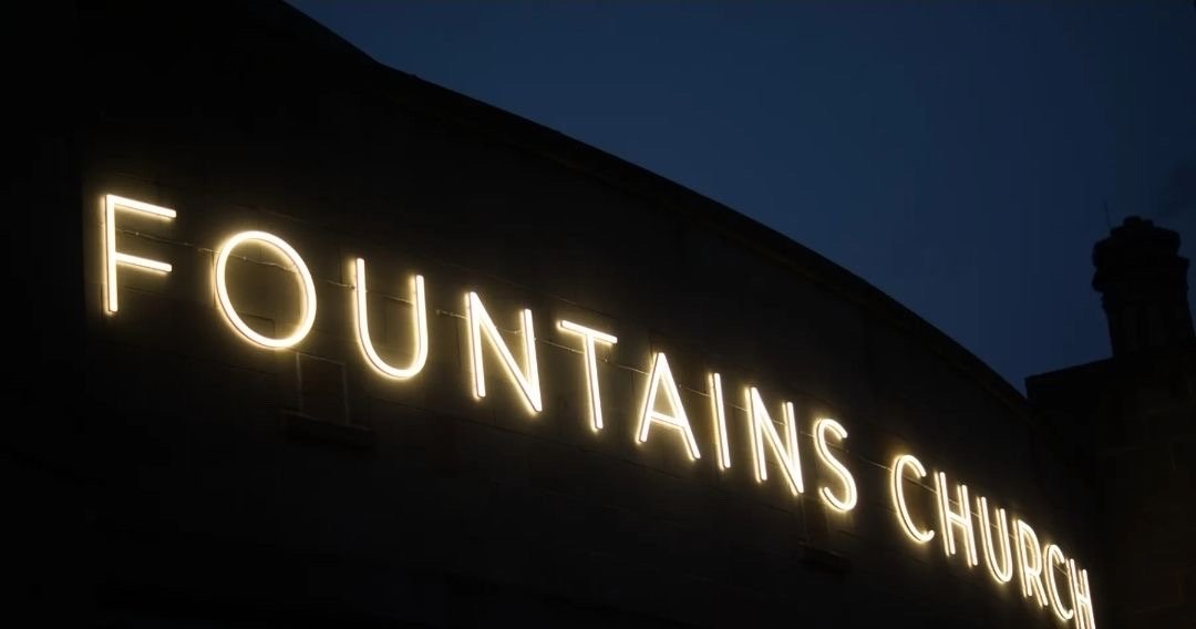 The illuminated Fountains Church sign on the building exterior at dusk